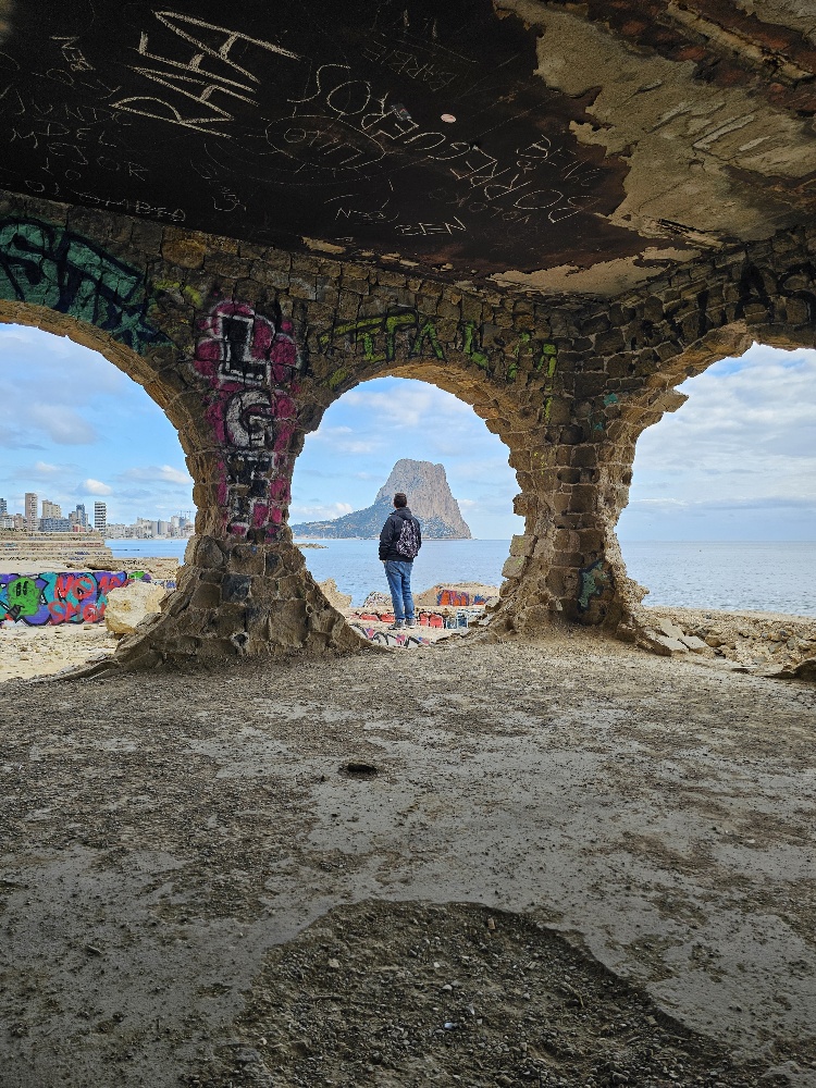 Kevin kijkt door een rond raam van de verlaten bar la manzanera in calpe spanje